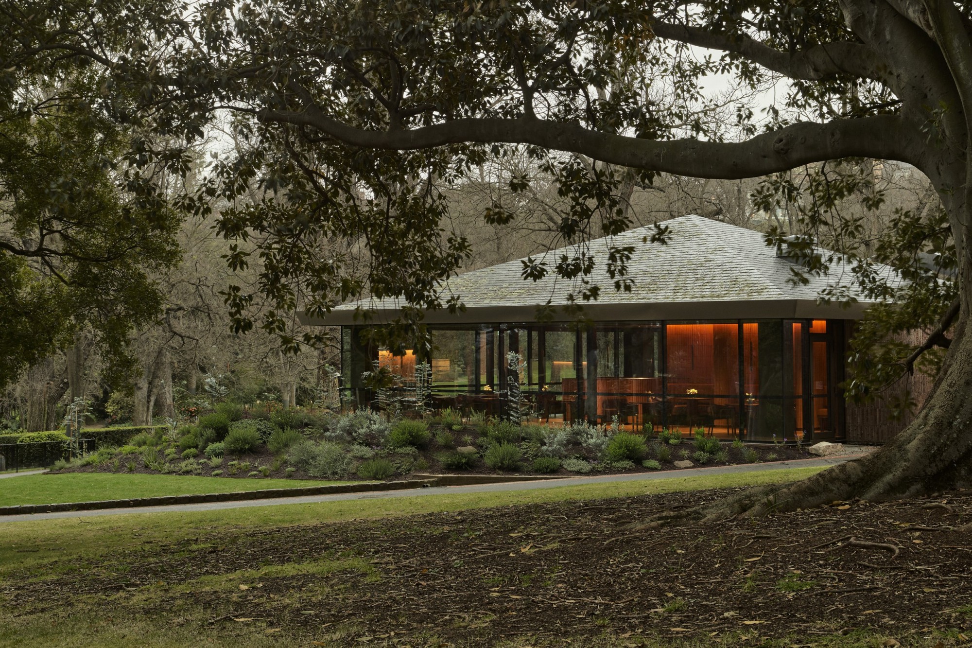 Photo of Yiaga, a contemporary pavilion-style building set within a landscaped garden, surrounded by mature trees and greenery.