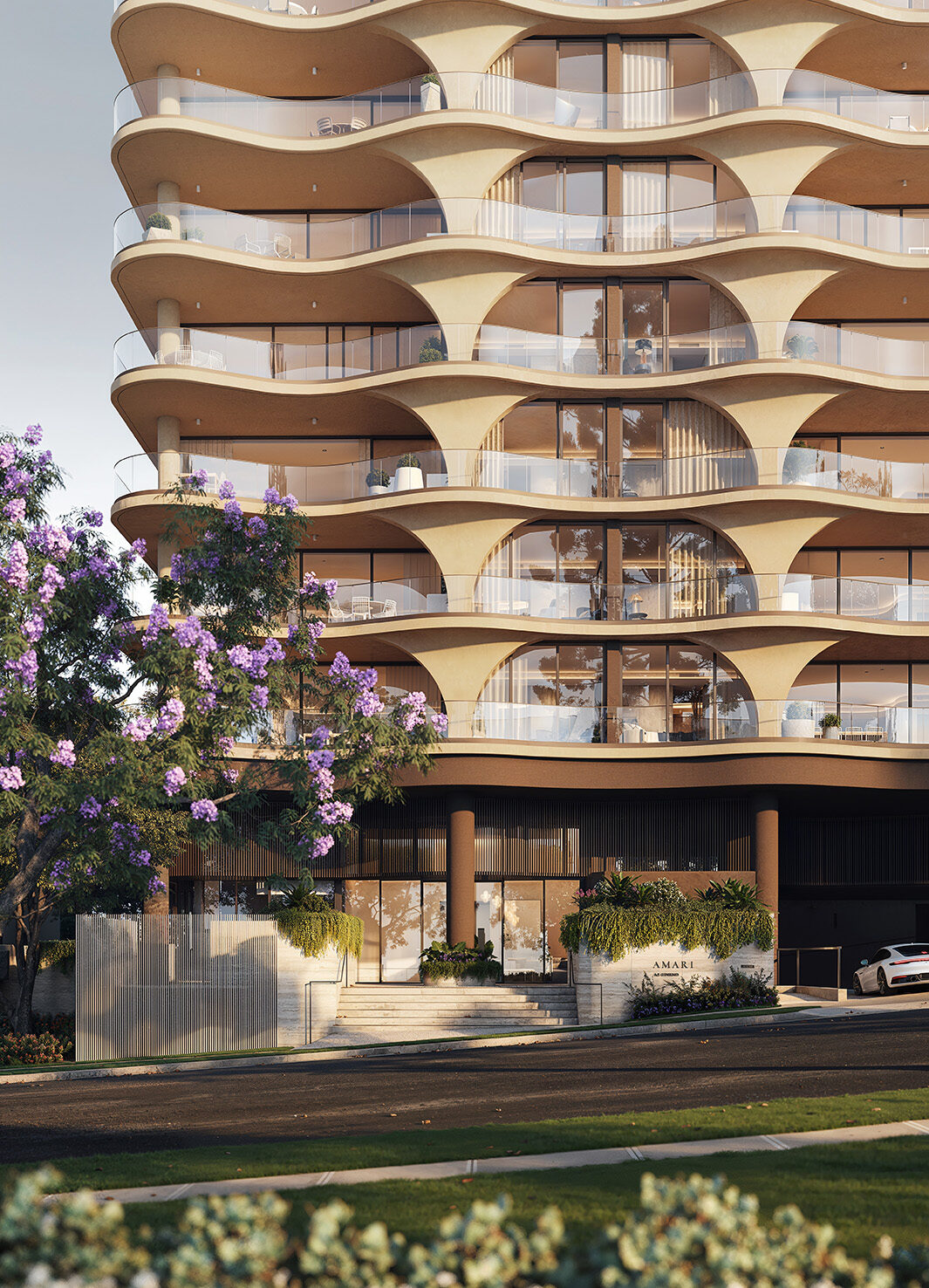 Curved, wave-like concrete balconies form a rhythmic, sunlit facade on a modern residential building, with glass railings, a planted street-level entrance and a purple-flowering tree in the foreground.