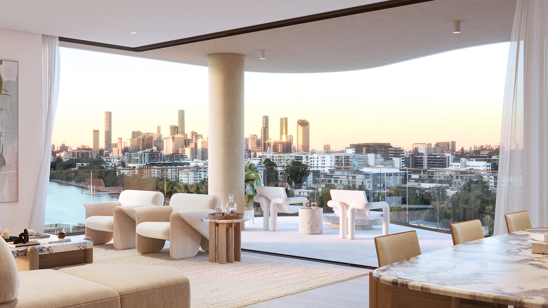 Open-plan luxury living room opening onto a glass-walled balcony with contemporary lounge chairs and tables, overlooking a river and a sunlit city skyline at sunset.